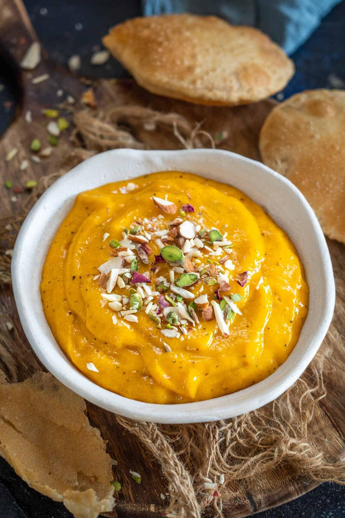 Aamras 2 Aamras servito in una ciotola, guarnito con mandorle a lamelle e pistacchi.