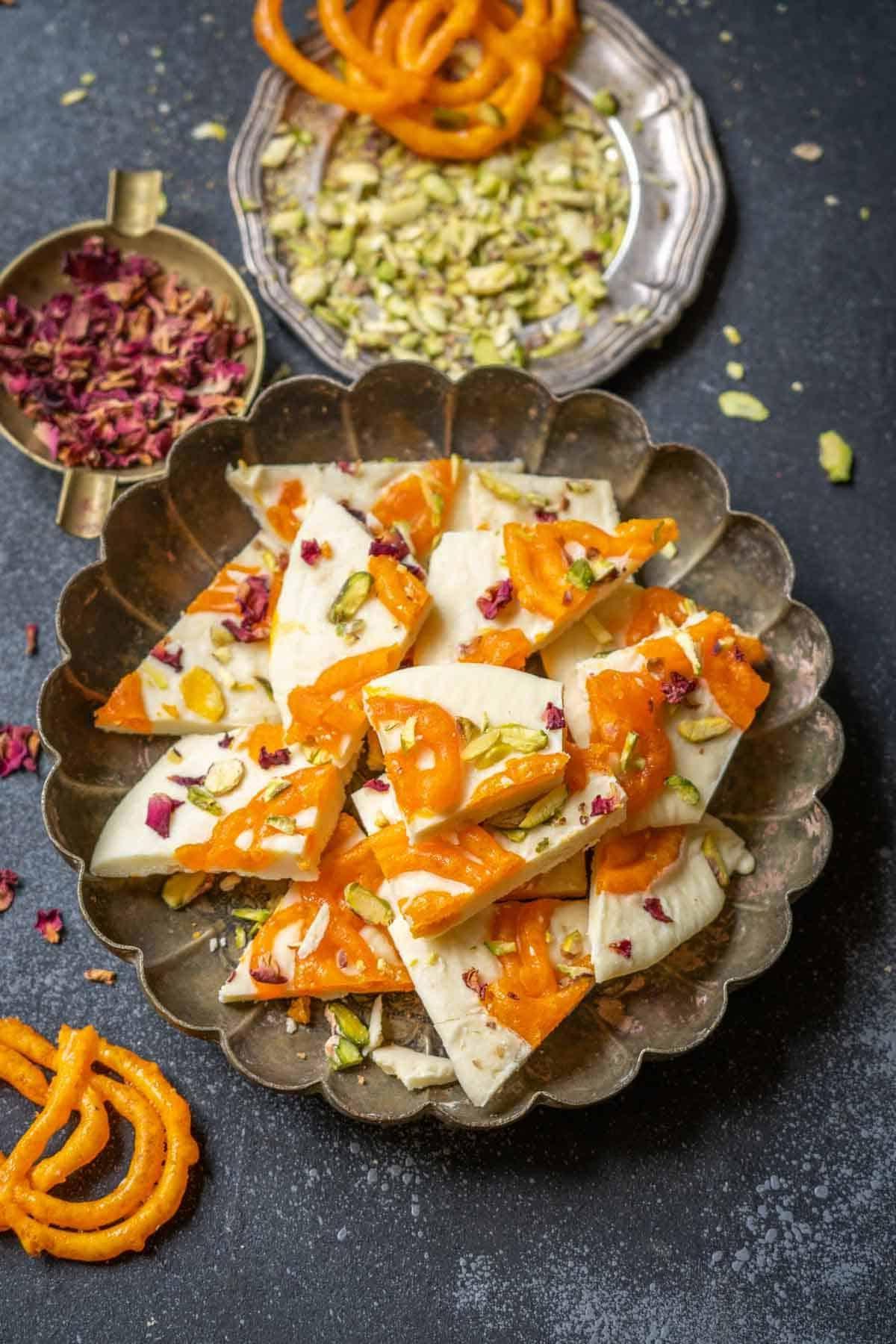 Scorza di Cioccolato Bianco al Jalebi 2 Pezzi di Cioccolato Bark di Jalebi e Cioccolato Bianco serviti su un piatto con petali di rosa.