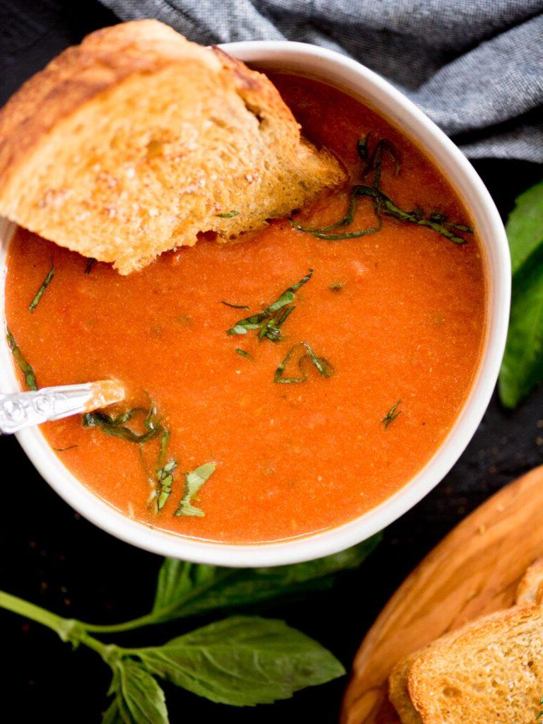 Zuppa Cremosa di Pomodori Arrostiti e Basilico 2 Una zuppa di pomodoro e basilico arrosto in una ciotola guarnita con basilico e un toast al formaggio immerso