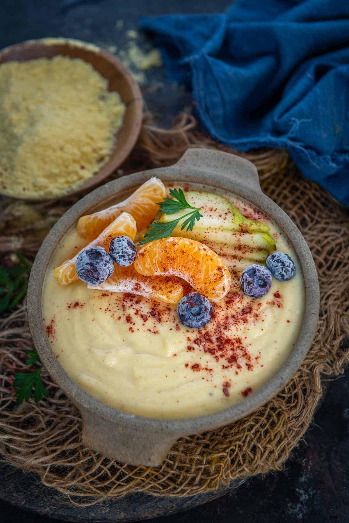 Porridge Giamaicano di Mais 2 Porridge di farina di mais giamaicano cremoso servito in una ciotola, guarnito con frutta fresca tropicale per una colazione vibrante.