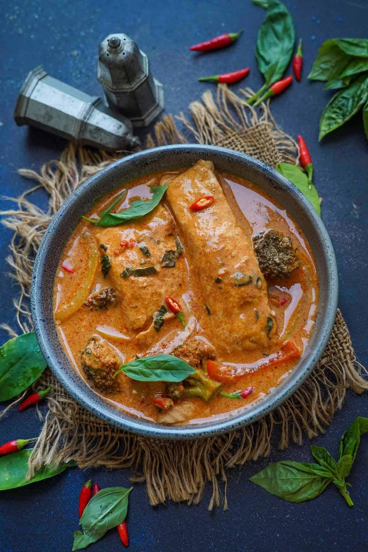 Salmone al Curry Panang 2 Curry Panang al Salmone servito in una ciotola, guarnito con peperoncini rossi affettati e foglie fresche di basilico thailandese.
