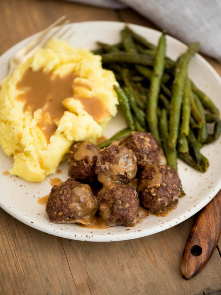 Polpette di cipolla alla francese servite su un piatto con purè di patate, salsa e fagiolini arrostiti