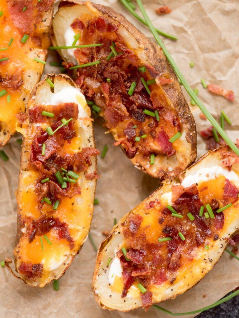 Facili Bucce di Patate in Friggitrice ad Aria 2 Bucce di patate cariche di formaggio, pancetta ed erba cipollina su carta forno, pronte da gustare.