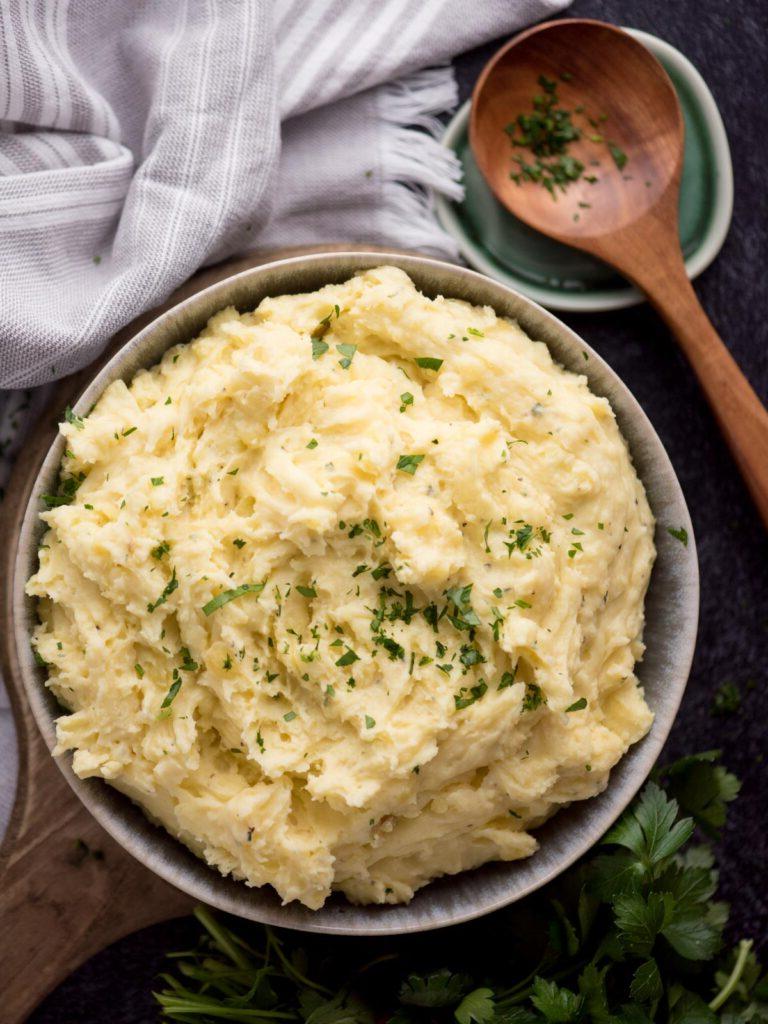 Purè di patate al Boursin 2 Una ciotola di purè di patate al Boursin servita, accanto a un poggia-cucchiaio di legno.