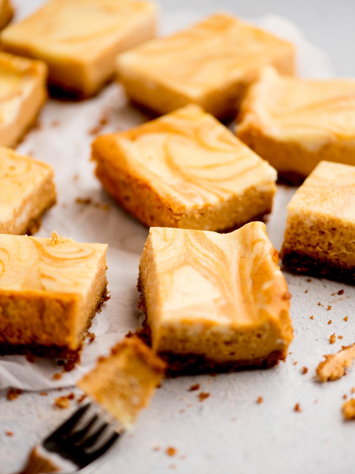 Come preparare i Quadrotti di Cheesecake alla Zucca 2 Barrette di cheesecake alla zucca su carta da forno con un morso su una forchetta
