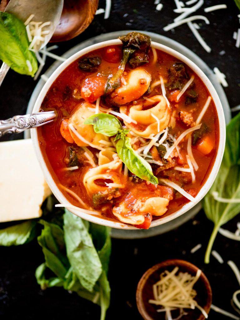 Tortellini al Pomodoro alla Fiorentina 2 Una ciotola di zuppa fiorentina di spinaci e tortellini, guarnita con parmigiano grattugiato e basilico fresco.