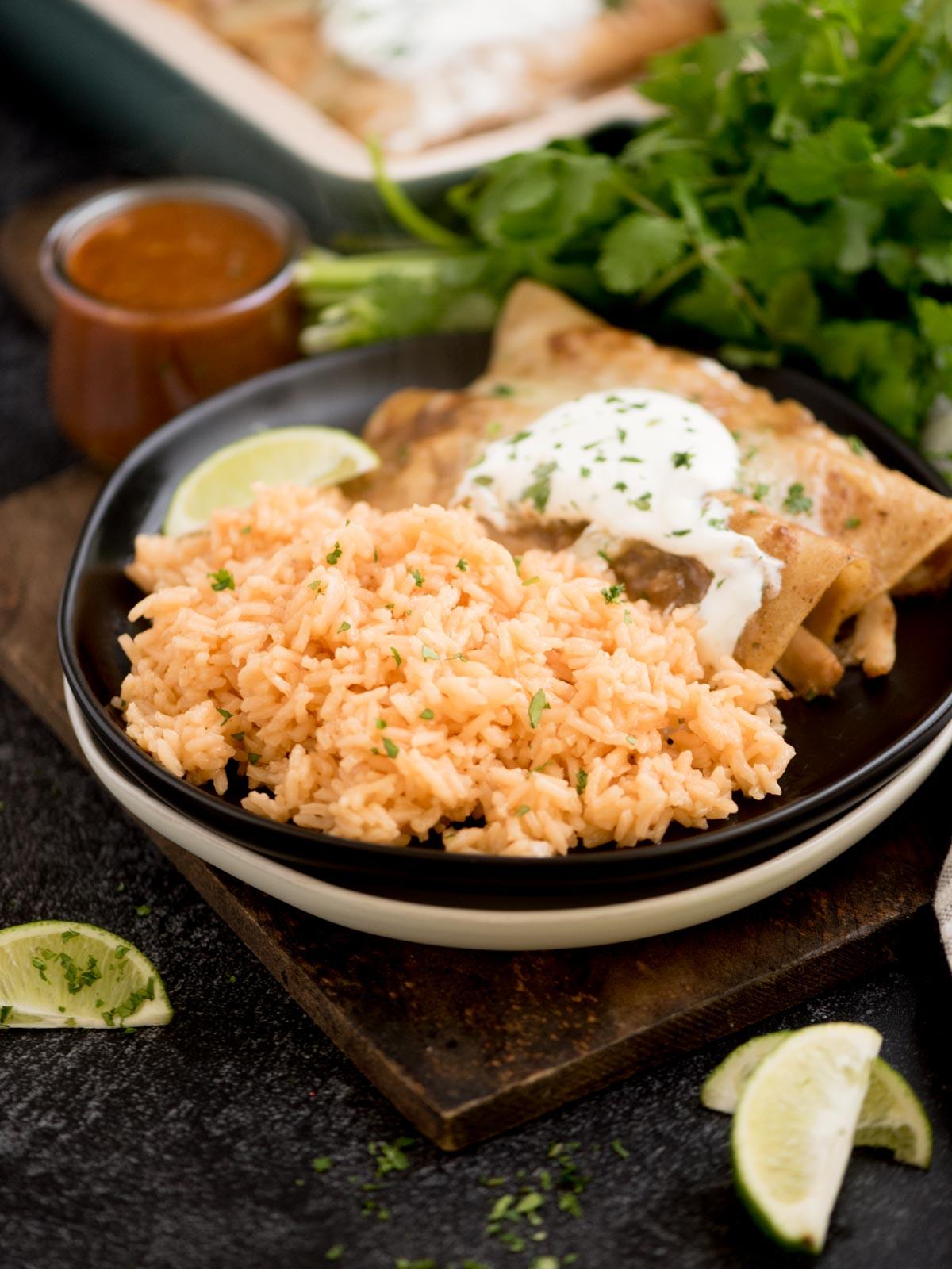 Riso Spagnolo Fatto in Casa 2 riso spagnolo su un piatto con enchiladas guarnite con coriandolo tritato su un tagliere di legno