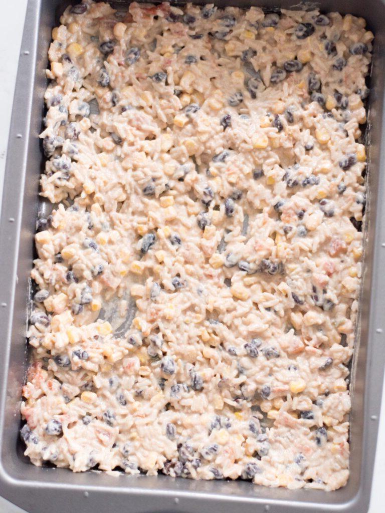 Sformato di Pollo Tex-Mex, Fagioli Neri e Riso 11 Pirofila da forno rettangolare con il primo strato di miscela di riso e verdure già distribuito uniformemente sul fondo.