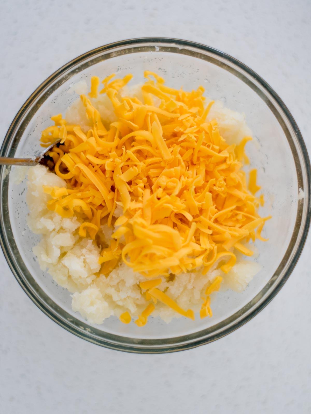 Patate Doppia Cottura in Friggitrice ad Aria 11 Patate e formaggio grattugiato aggiunti a una ciotola per le patate ripiene.