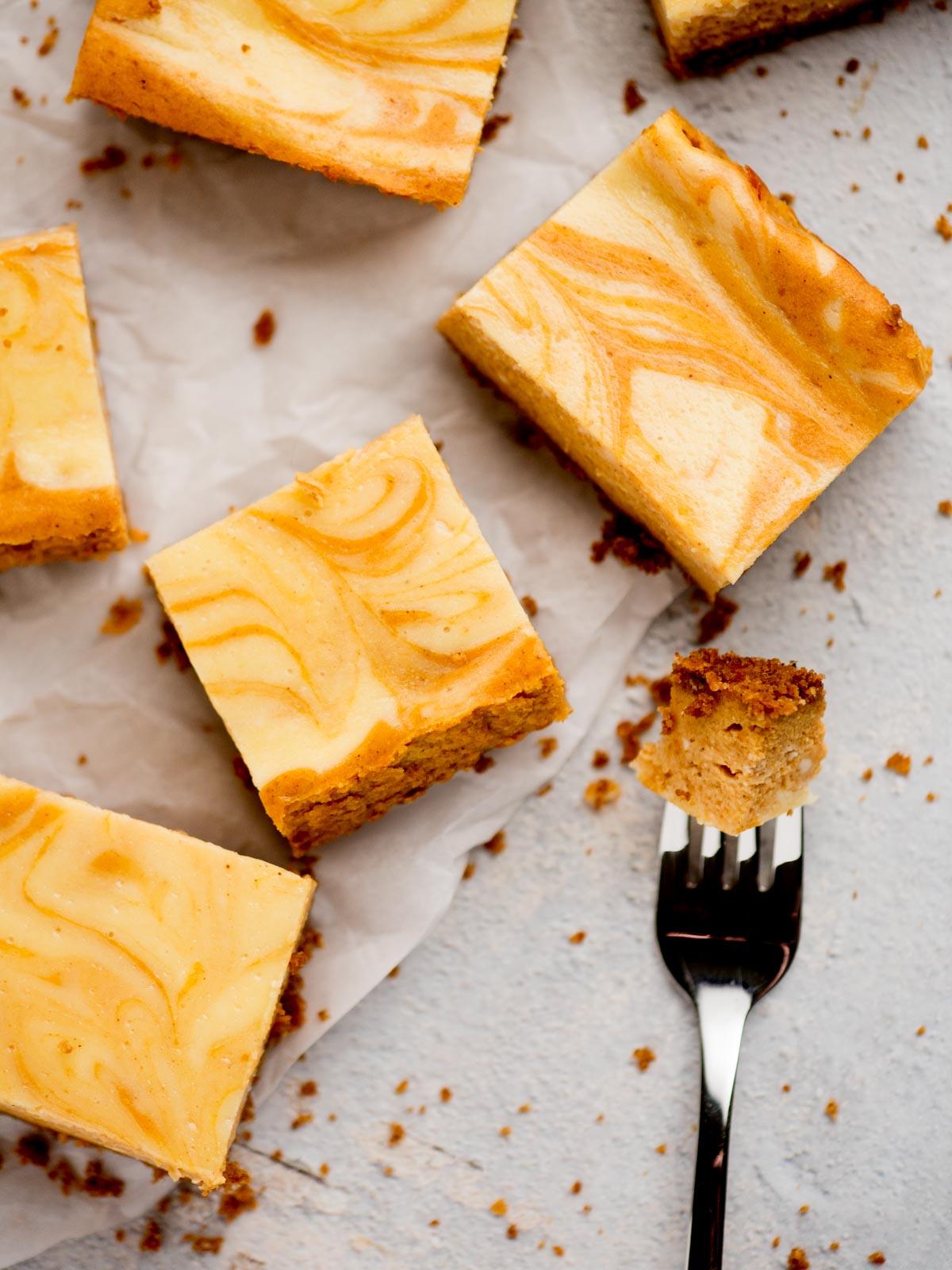 Come preparare i Quadrotti di Cheesecake alla Zucca 12 Barrette di cheesecake alla zucca su carta da forno con un morso su una forchetta