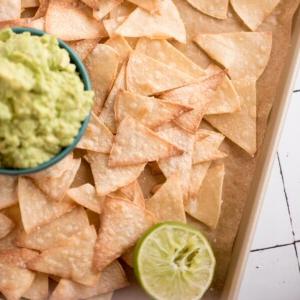 Deliziose chips fatte in casa al forno su un vassoio di servizio con un contorno di guacamole e mezzo lime spremuto.