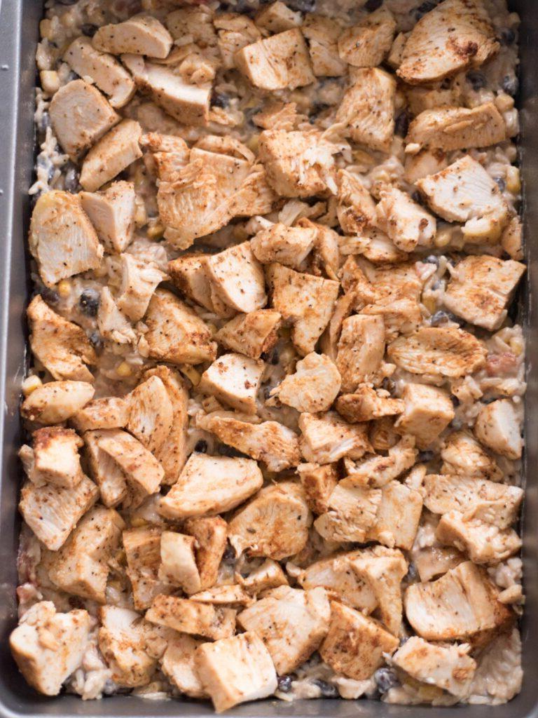 Sformato di Pollo Tex-Mex, Fagioli Neri e Riso 12 Strato di pollo condito uniformemente distribuito sopra il primo strato di miscela di riso nella pirofila da forno.