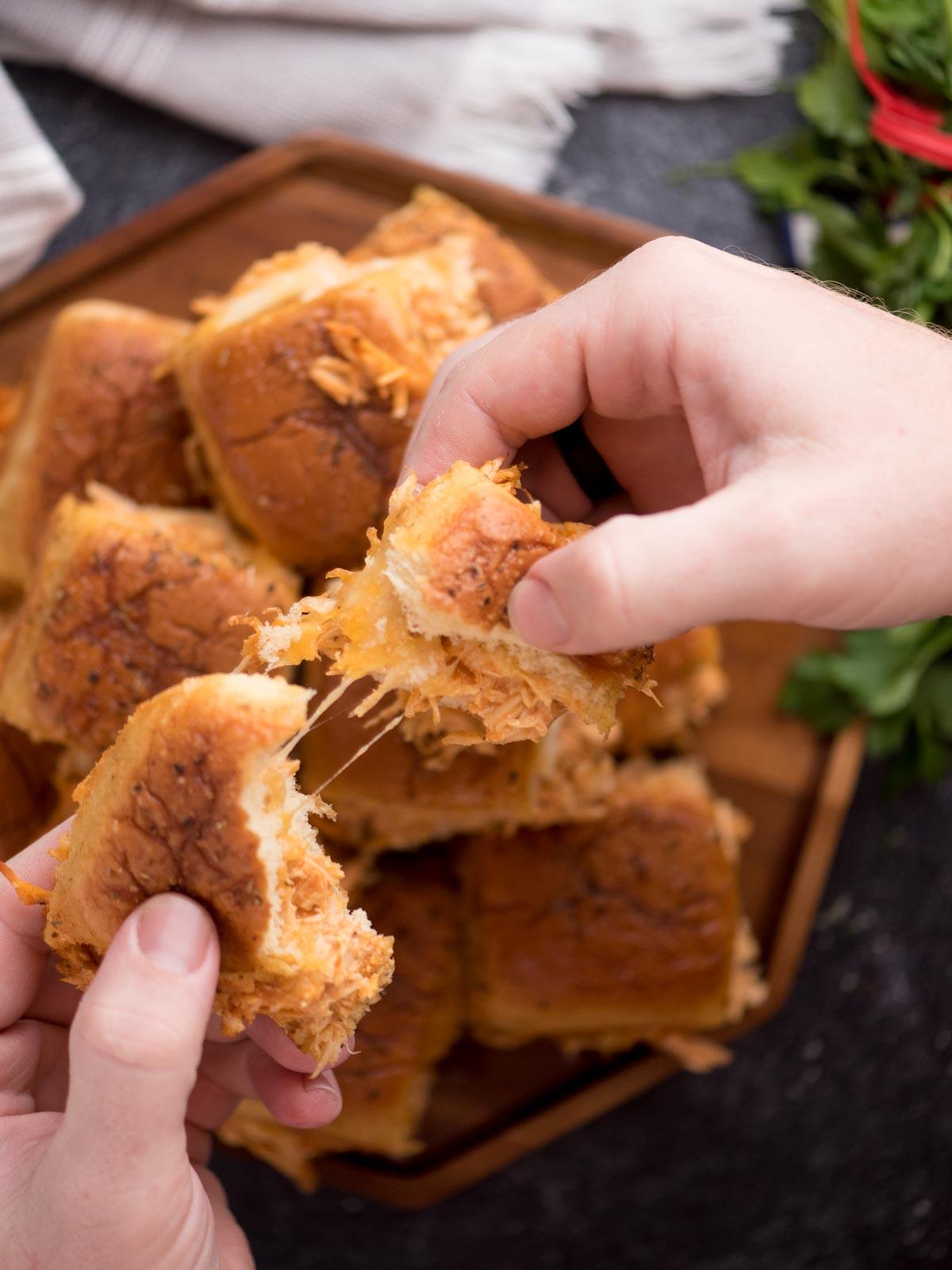 Mini-panini Hawaiani al Pollo Buffalo 14 Mano che separa uno slider di pollo Buffalo formaggioso.