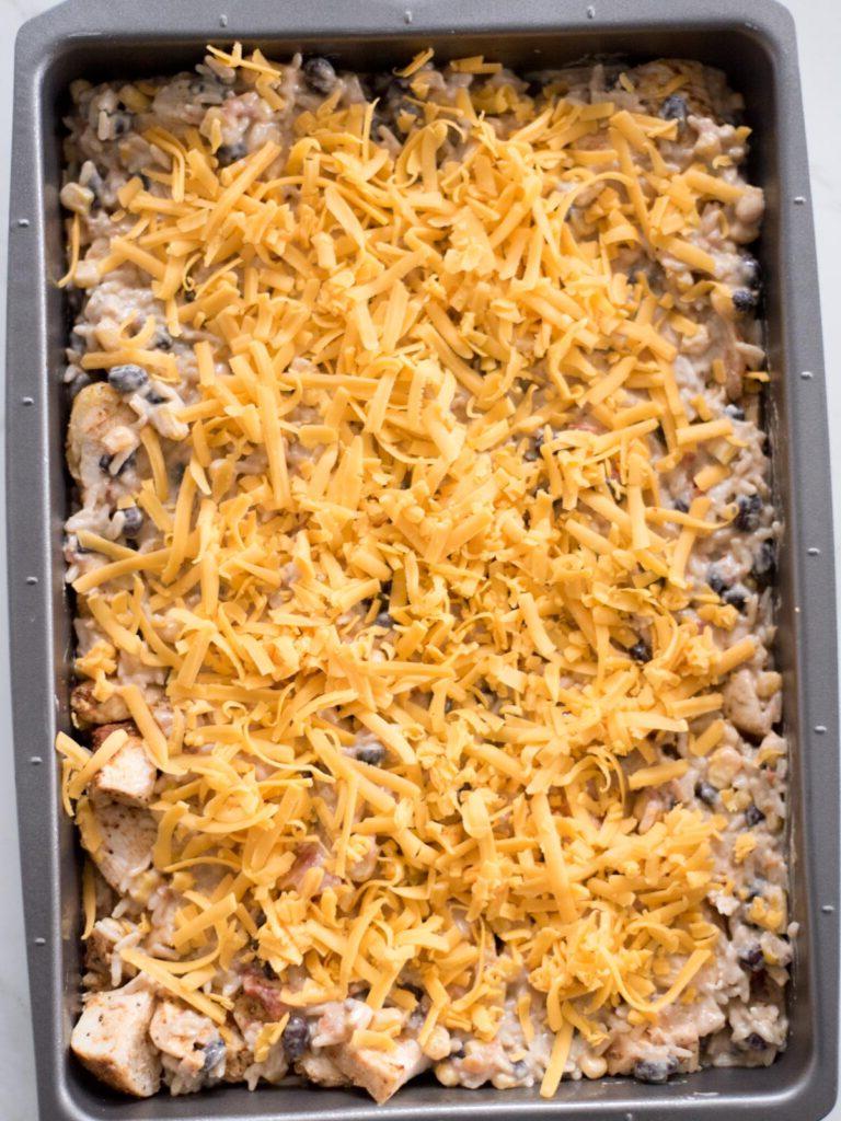 Sformato di Pollo Tex-Mex, Fagioli Neri e Riso 14 Formaggio grattugiato misto (Monterrey Jack e Cheddar) abbondantemente cosparso sopra l'ultimo strato di riso nella pirofila, pronto per la cottura.