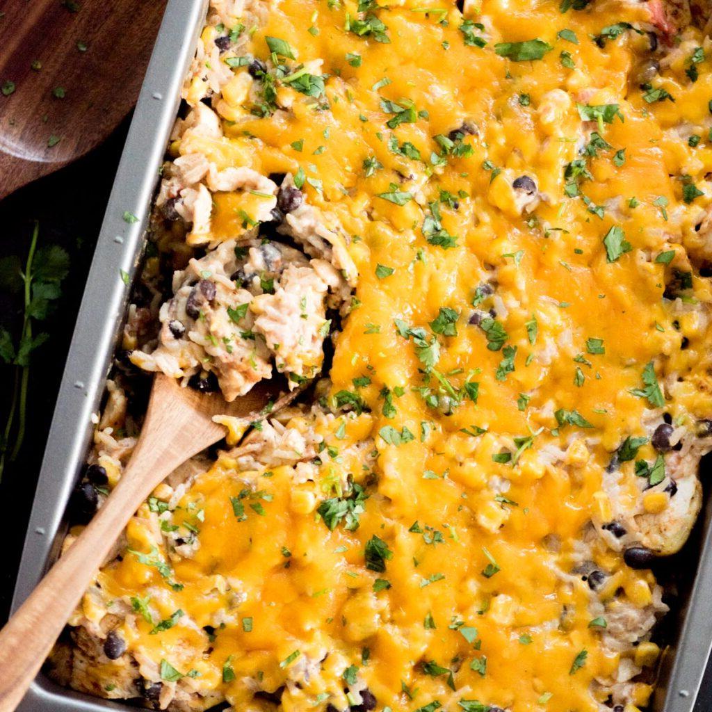 Sformato di Pollo Tex-Mex, Fagioli Neri e Riso 3 Cucchiaio di legno che serve una porzione di teglia di pollo Tex-Mex con fagioli neri direttamente dalla pirofila da forno.
