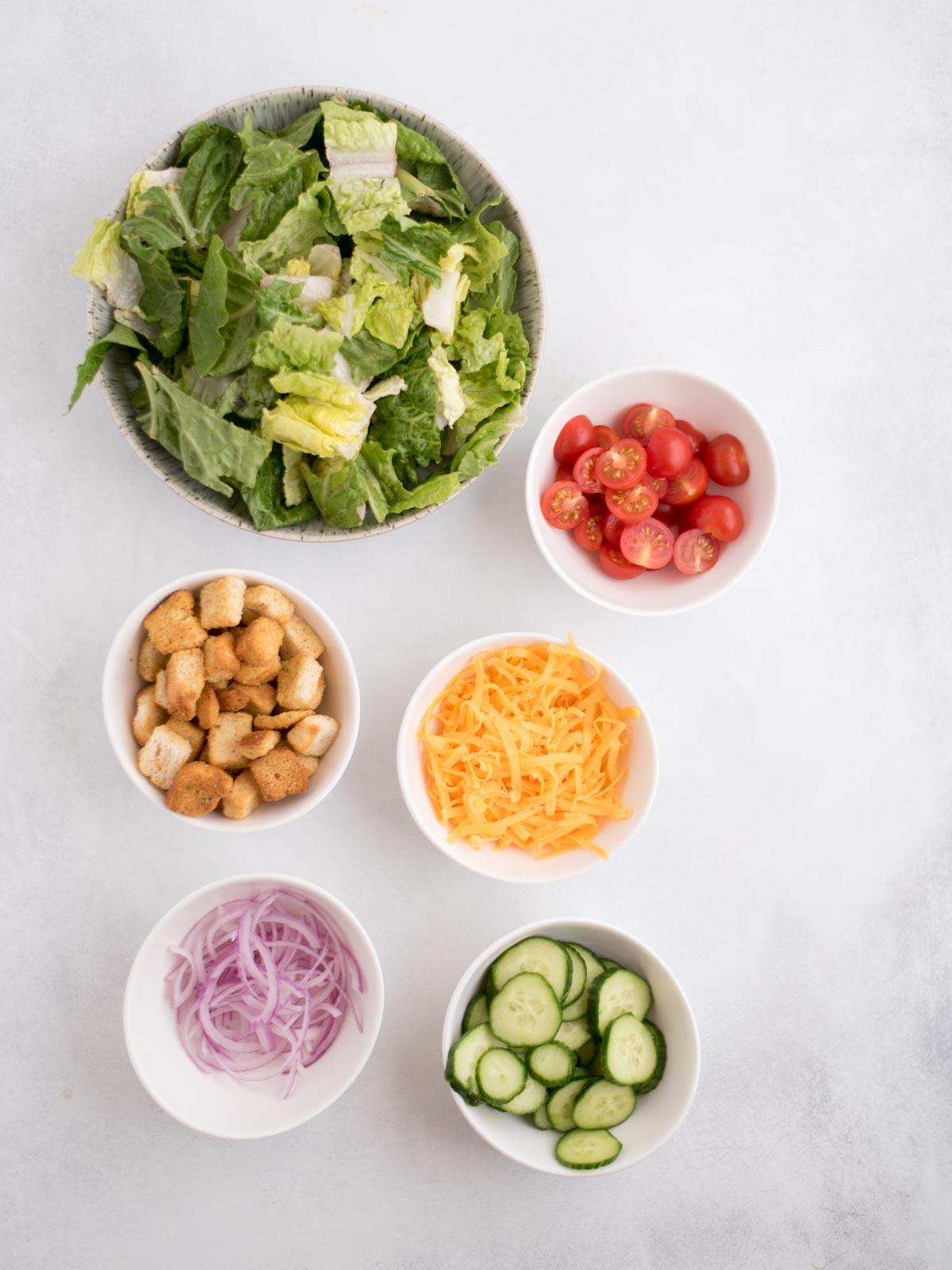 Ricetta Insalata della Casa 3 Ingredienti freschi per preparare un'insalata di casa: lattuga, pomodori, cetrioli, cipolla rossa, formaggio cheddar e crostini.