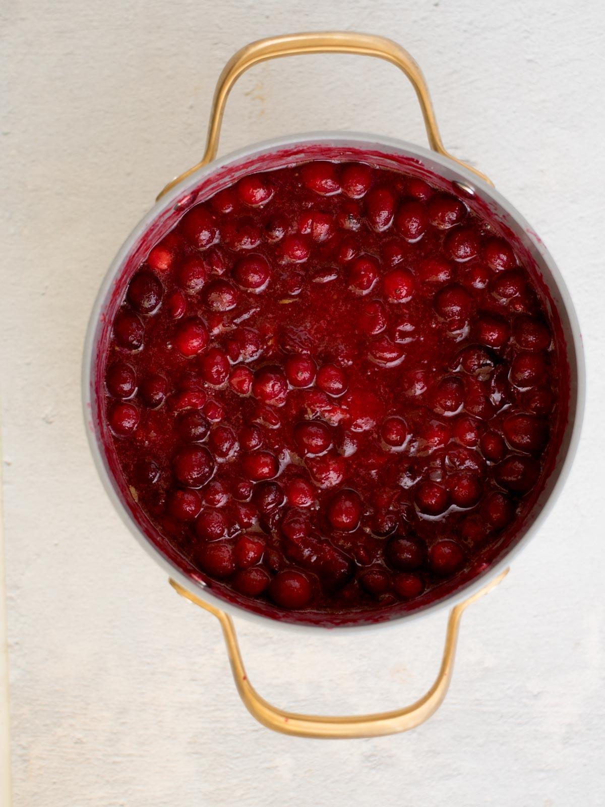 Salsa ai Mirtilli Rossi Interi 4 Una pentola piena di salsa di mirtilli rossi di colore rosso vibrante, con mirtilli interi e una consistenza lucida, su uno sfondo chiaro. La pentola ha manici dorati, aggiungendo un tocco decorativo alla presentazione semplice.