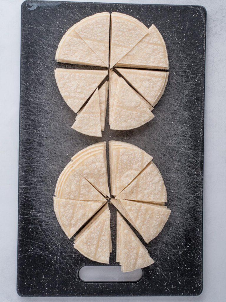 Tagliere con pile di tortillas di mais tagliate a triangoli in preparazione per fare chips fatti in casa.