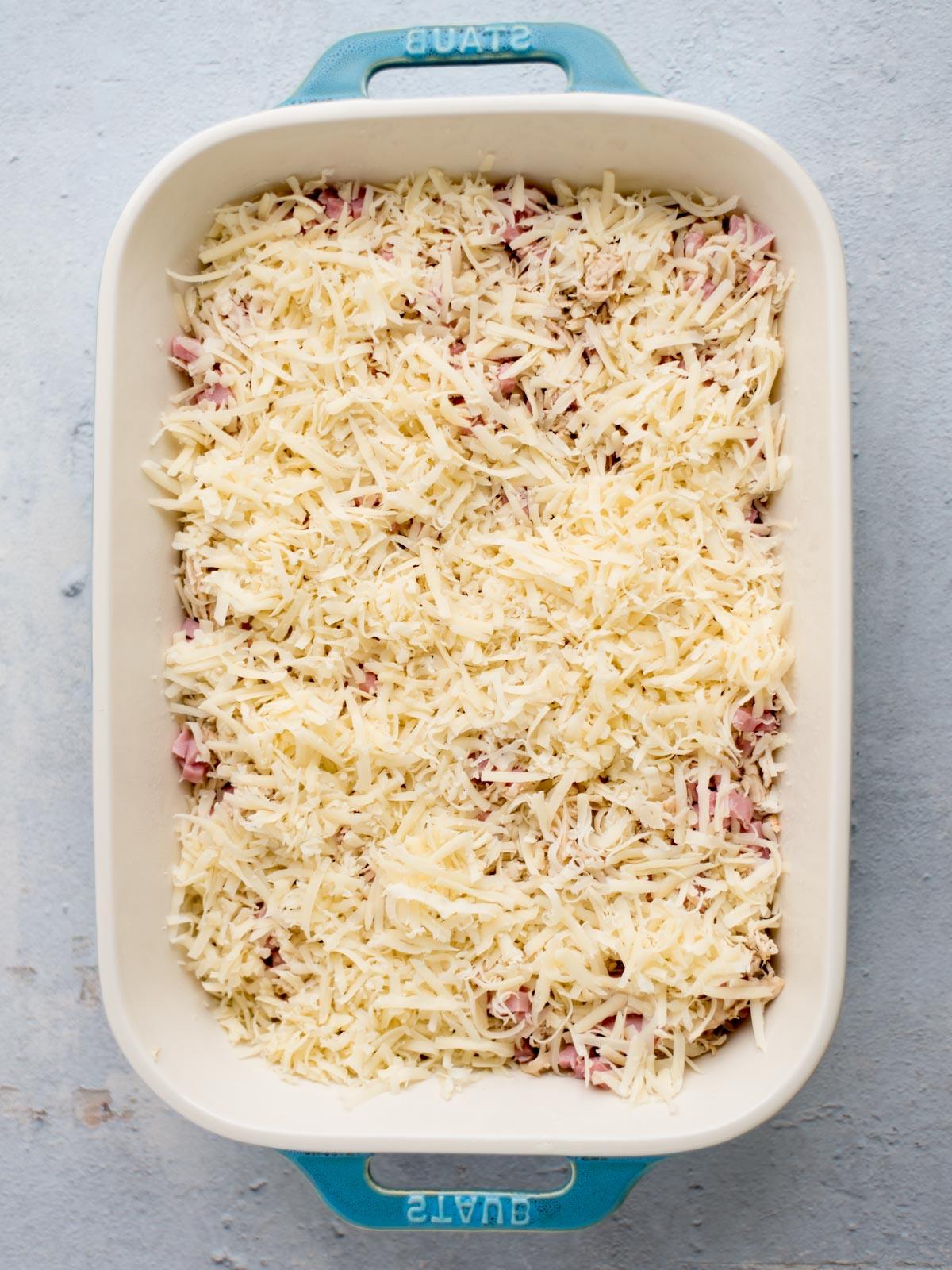 Fasi di assemblaggio della teglia di pollo cordon bleu: pollo, prosciutto e formaggio svizzero nella teglia da forno.
