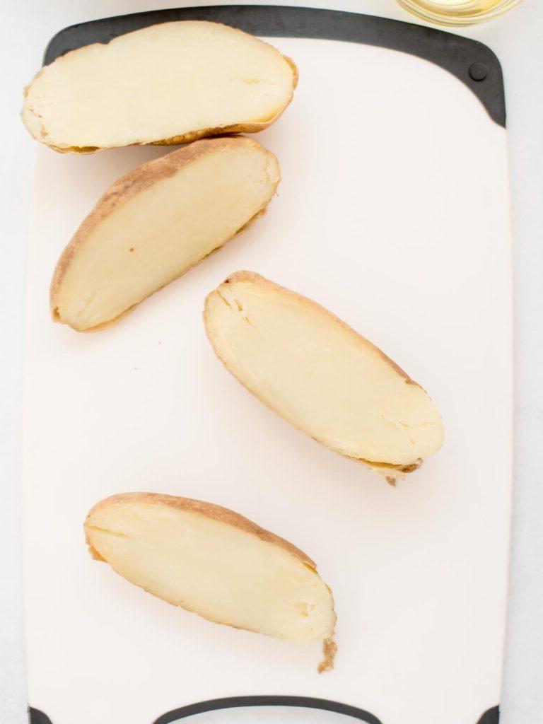 Facili Bucce di Patate in Friggitrice ad Aria 4 2 patate russet tagliate a metà e appoggiate su un tagliere, pronte per essere preparate per le bucce di patate.