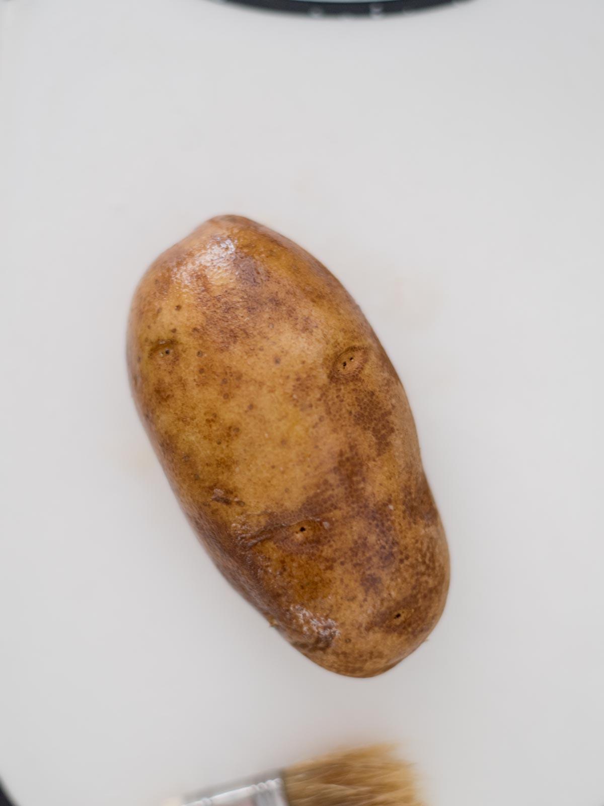 Patate Doppia Cottura in Friggitrice ad Aria 4 Una patata intera lavata e forata con i rebbi di una forchetta.