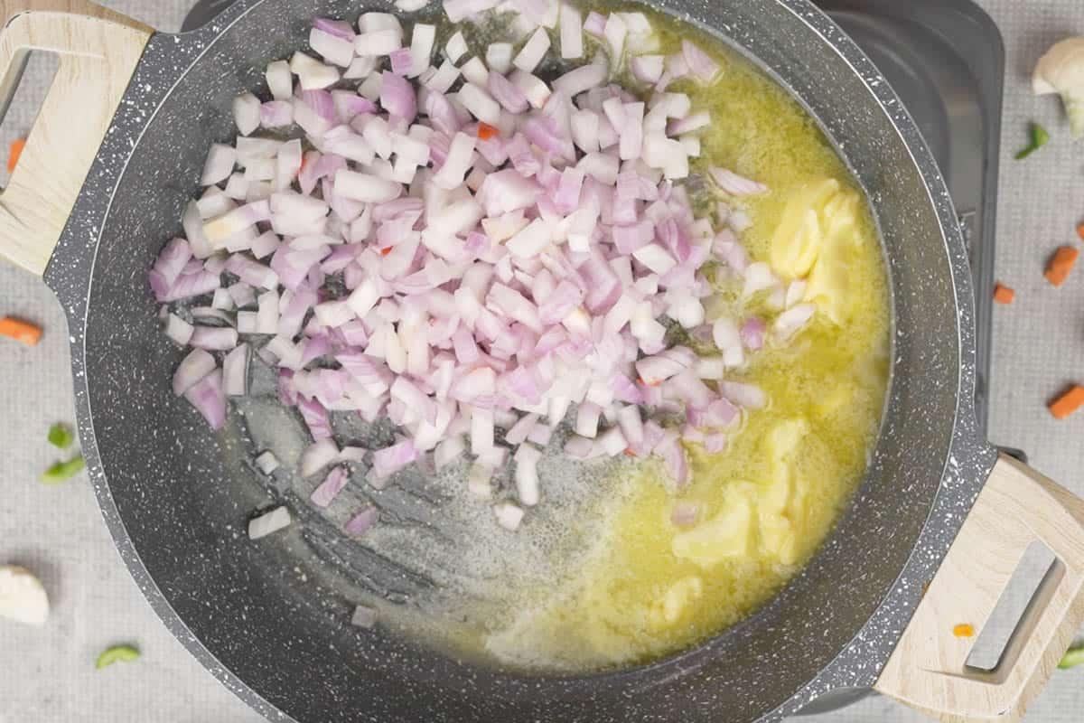 Cipolle tritate aggiunte al burro caldo in una padella, pronte per essere soffritte.
