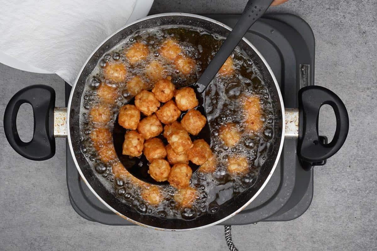 Tater tots che friggono in olio caldo.