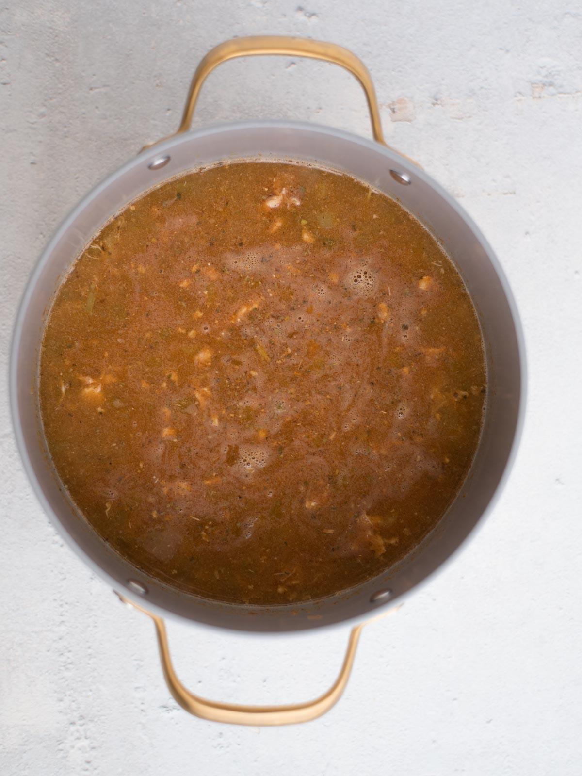 Chili di Pollo Bianco del Sud-Ovest 5 Una pentola piena di un saporito chili bianco di pollo, che sobbolle delicatamente per rivelare teneri pezzi di carne e verdure vivaci. La pentola, dotata di due robusti manici, poggia con grazia su una superficie grigio chiaro.