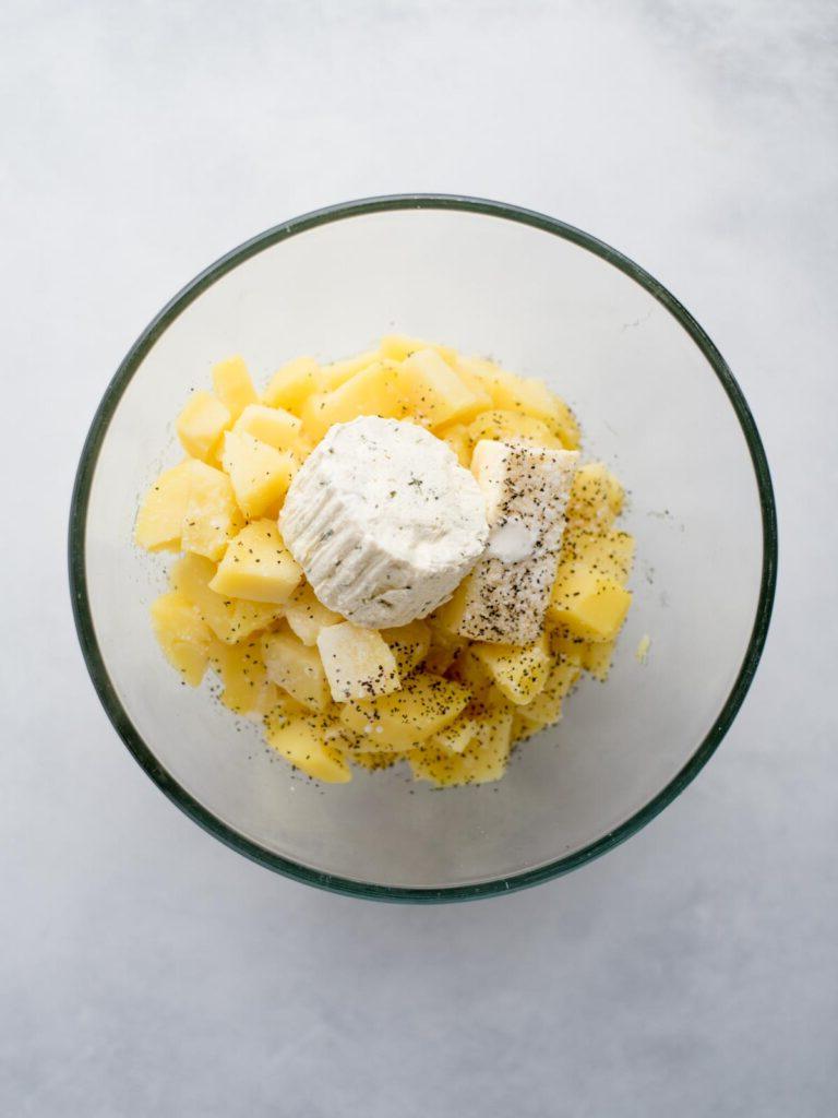 Purè di patate al Boursin 5 Patate cotte aggiunte a una ciotola con condimenti e formaggio Boursin aggiunti in cima.