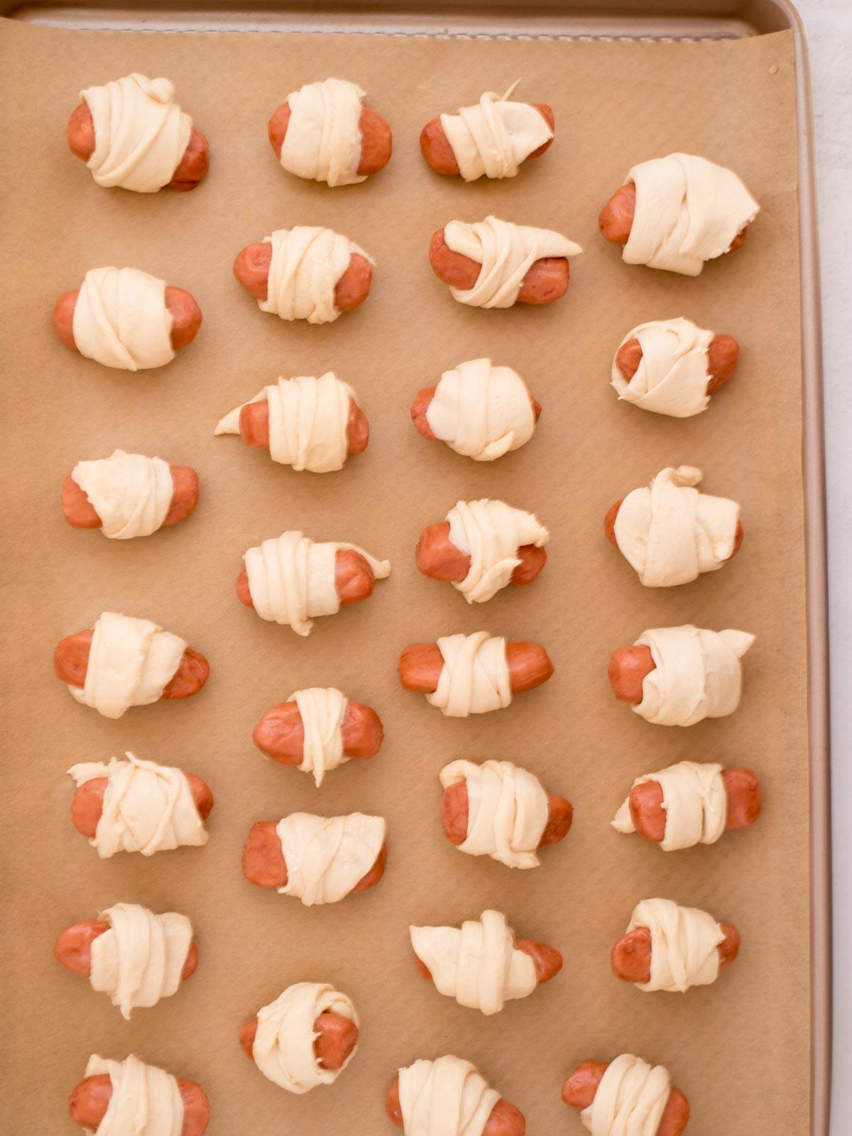 Mini Wurstel in Pasta Sfoglia 5 Mini wurstel affumicati avvolti nella pasta sfoglia su una teglia coperta di carta forno.