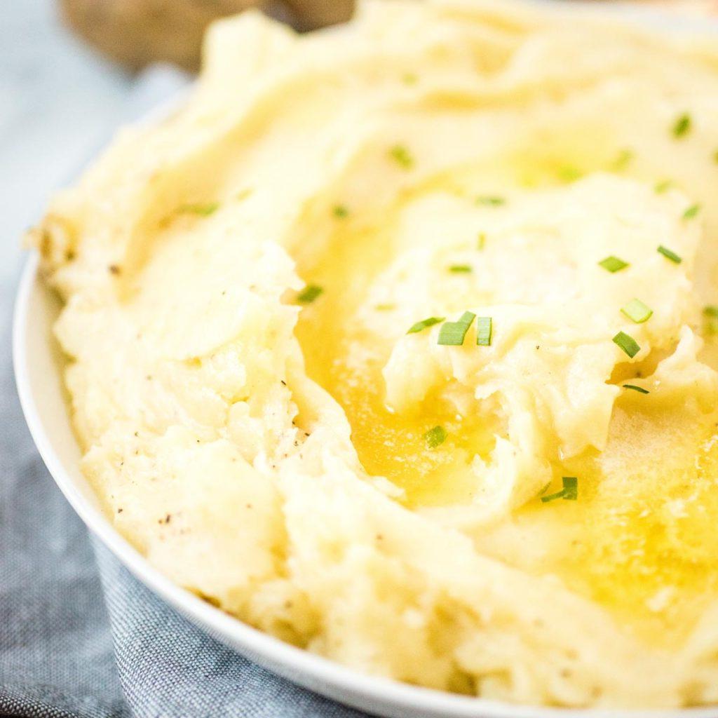 Ricette Instant Pot per il Ringraziamento 4 Purè di patate in una ciotola bianca guarnito con burro fuso ed erba cipollina