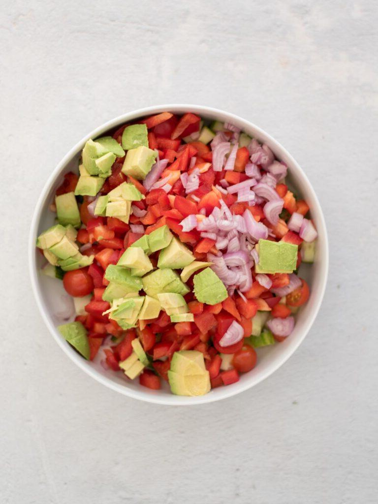 Insalata di Cetrioli, Pomodori, Cipolle e Avocado 5 Ingredienti tritati per l'insalata di cetrioli e pomodori in una ciotola prima di unire.