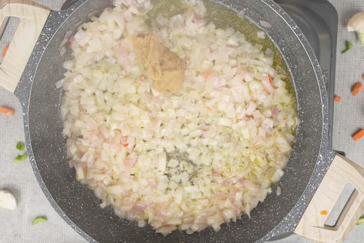 Pasta di zenzero e aglio aggiunta alla padella con le cipolle, pronta per essere soffritta.