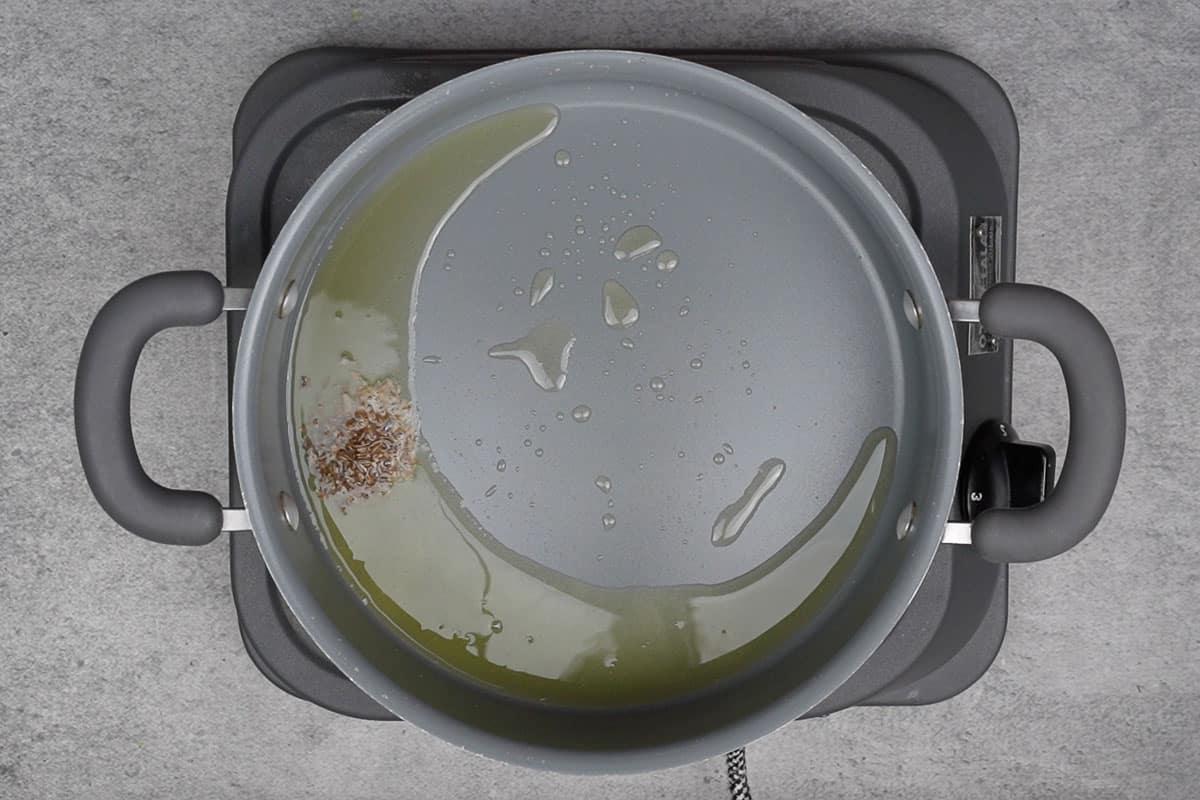 Semi di cumino aggiunti alla pentola, che scoppiettano nell'olio caldo.