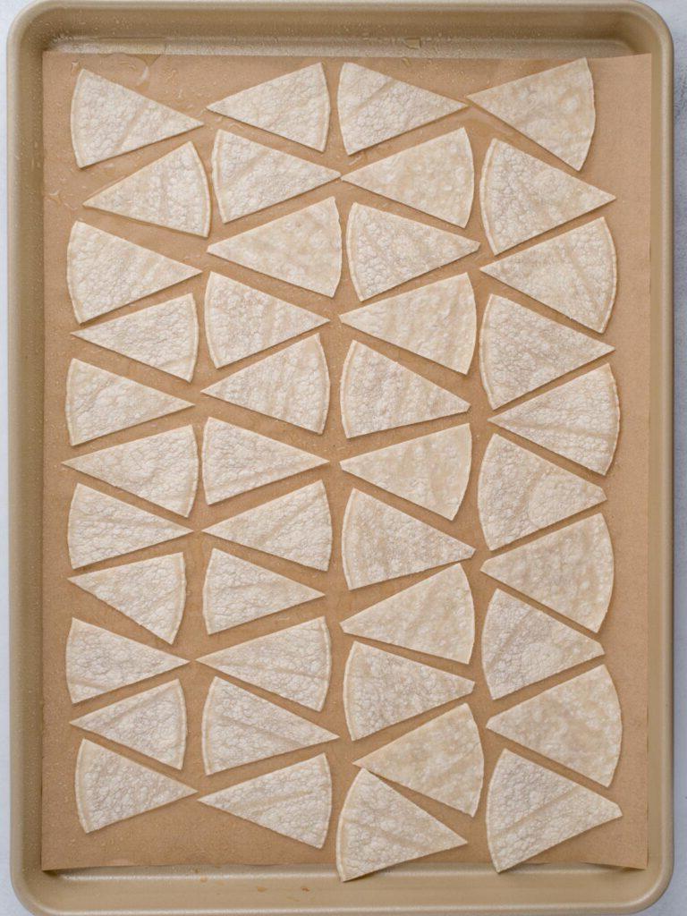 Tortillas di mais tagliate a triangoli e disposte su una teglia pronte per essere cotte.