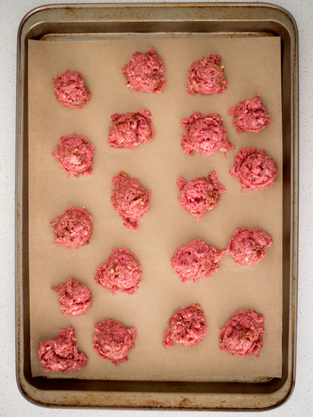 Polpette prelevate con un cucchiaio dosatore e disposte su una teglia da forno rivestita di carta forno