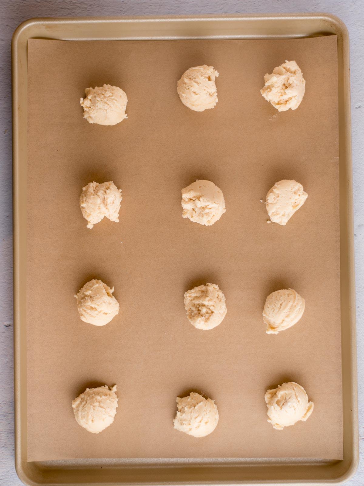 scooped balls of condensed milk cookie dough on a parchment lined baking sheet