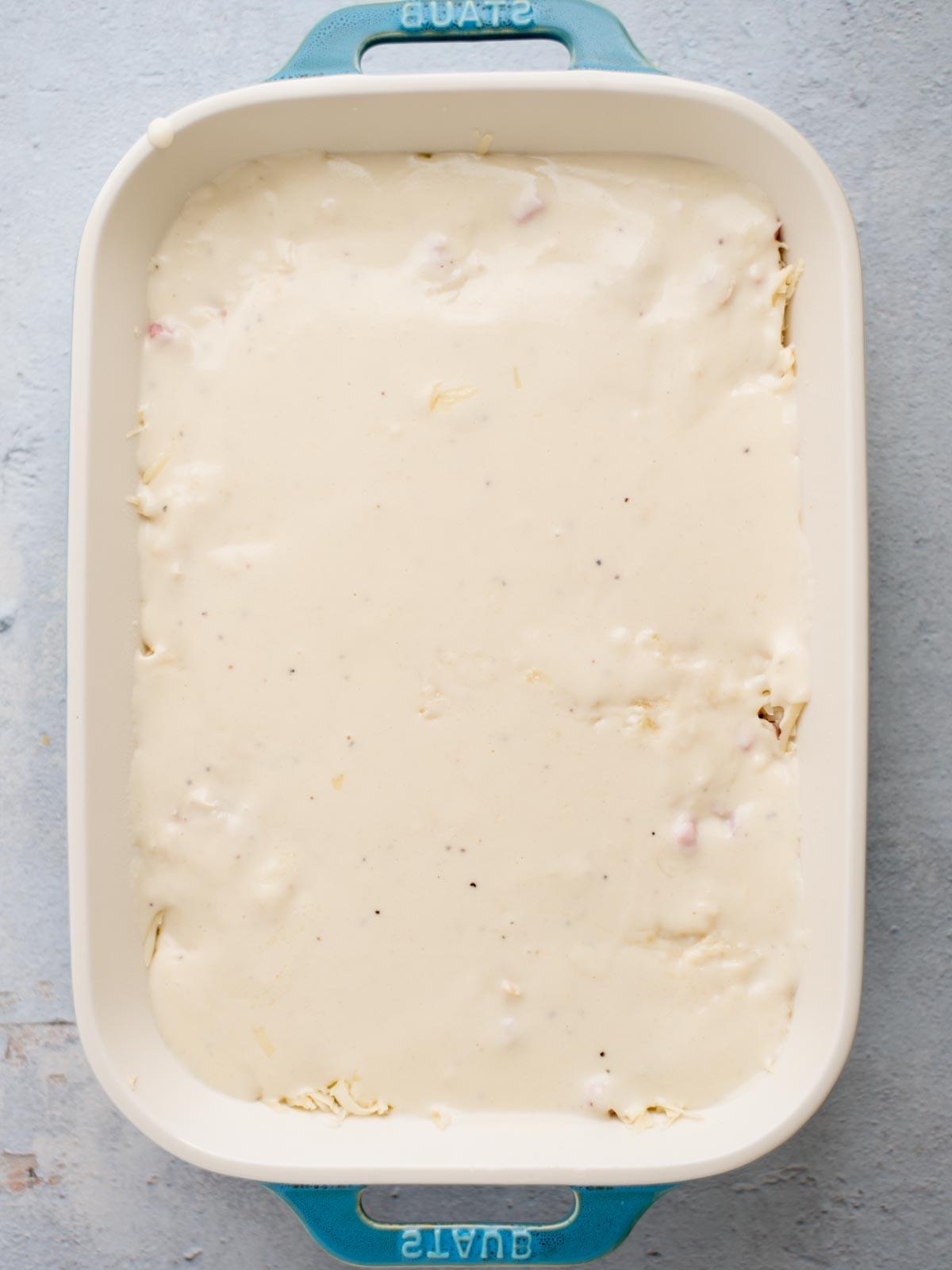 Fasi di assemblaggio della teglia di pollo cordon bleu: la salsa è stata versata sopra il formaggio svizzero.