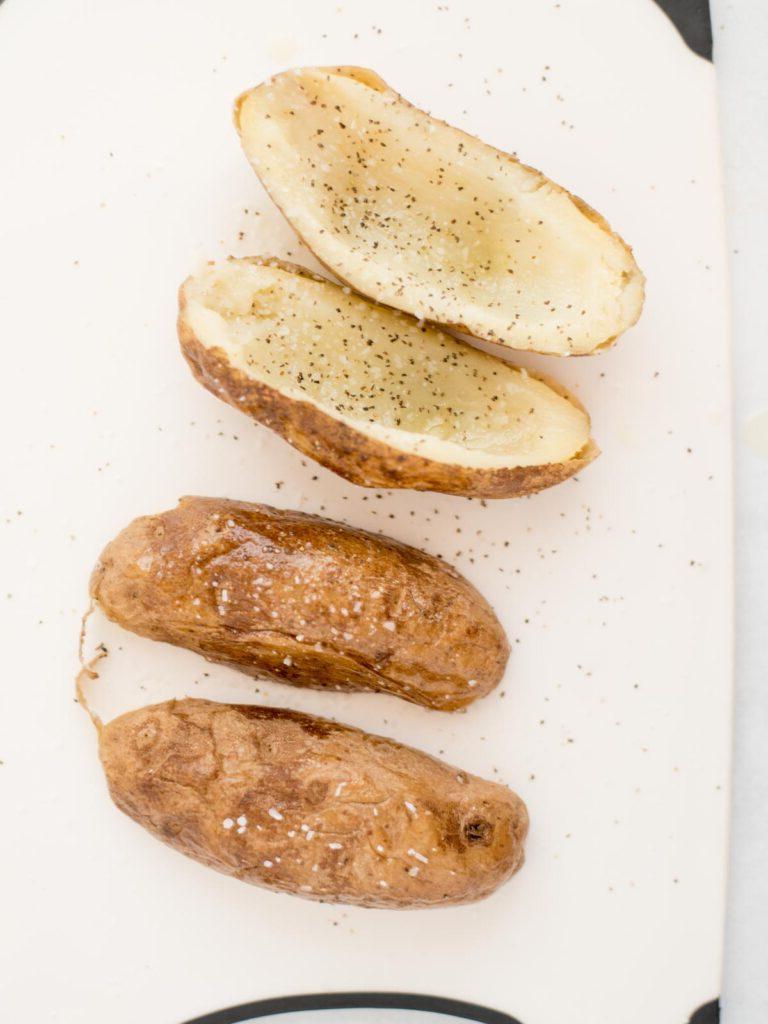 Facili Bucce di Patate in Friggitrice ad Aria 6 4 patate russet, 2 in verticale, 2 capovolte, appoggiate su carta forno, cosparse di sale e pepe su entrambi i lati della patata.