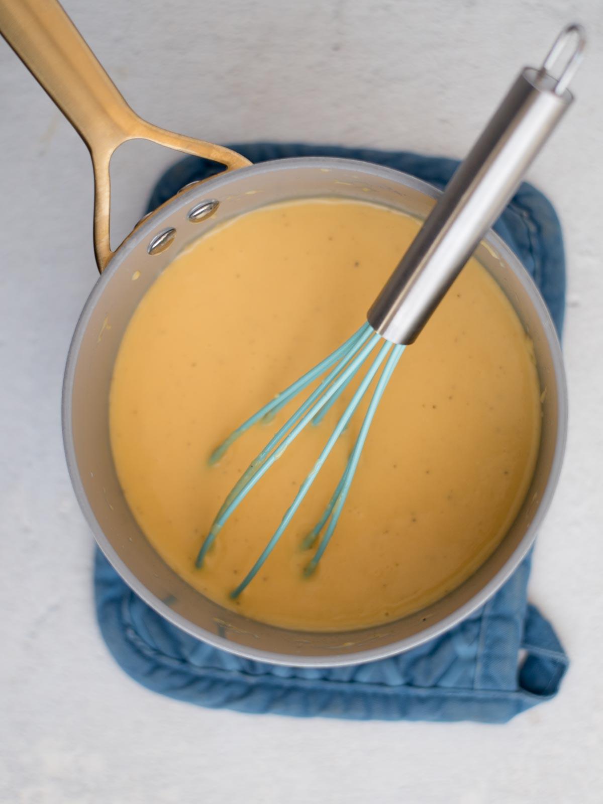 **I Migliori Maccheroni al Forno Super Formaggiosi** 6 Frusta da cucina appoggiata in una casseruola di salsa al formaggio cremosa.