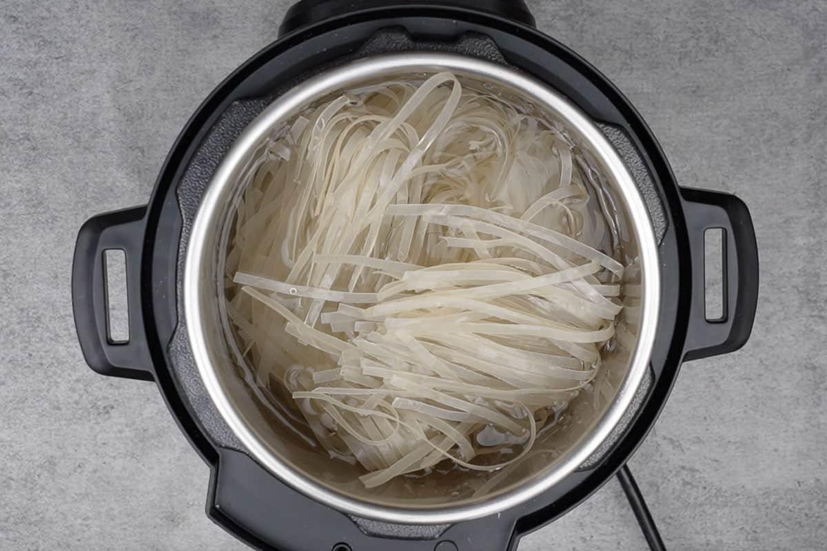 Instant Pot Pad Thai Vegetariano 7 Noodles messi nella pentola istantanea e coperti d'acqua.