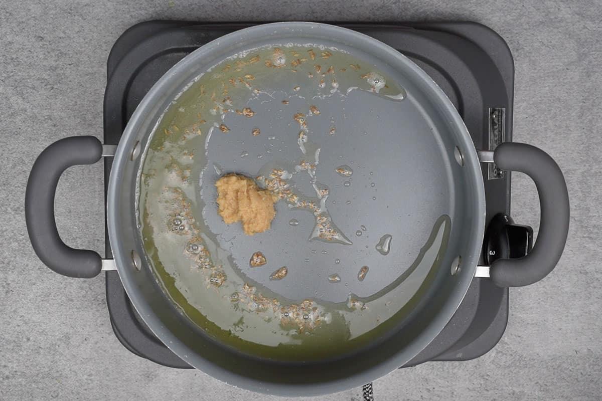 Pasta di zenzero e aglio aggiunta alla pentola, che frigge e rilascia i suoi aromi.
