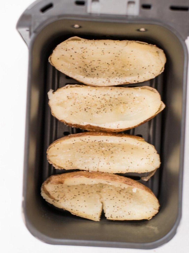 Facili Bucce di Patate in Friggitrice ad Aria 7 4 metà di patate svuotate aggiunte in un cestello della friggitrice ad aria che sono state cosparse di sale e pepe.