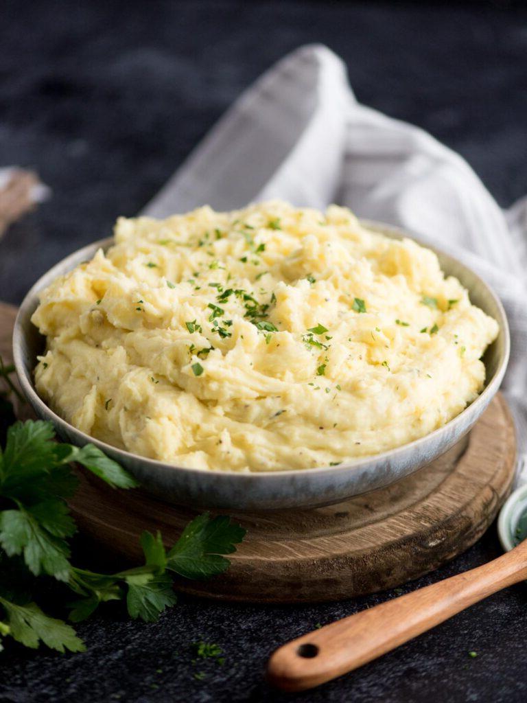 Purè di patate al Boursin 7 Prezzemolo guarnito accanto a una ciotola di purè di patate al Boursin.