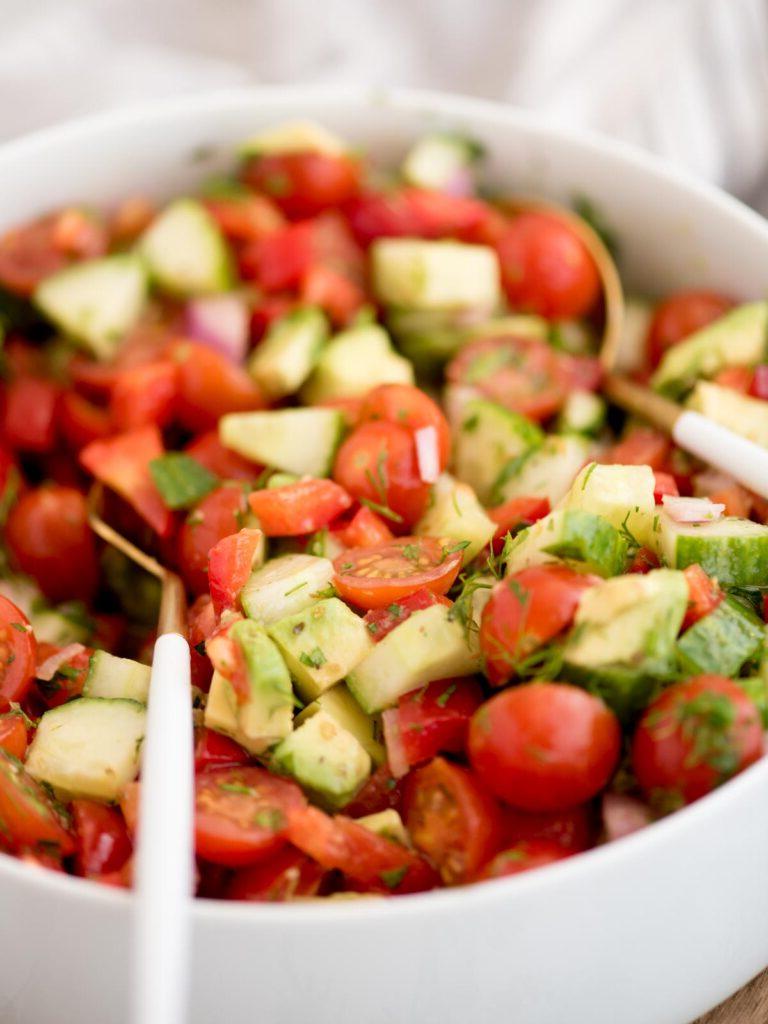Insalata di Cetrioli, Pomodori, Cipolle e Avocado 7 Grande ciotola di insalata di cetrioli e pomodori con un cucchiaio da portata appoggiato all'interno.