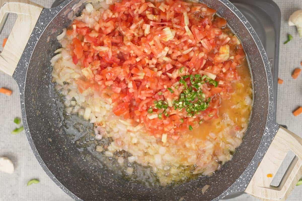 Peperoncini verdi, pomodori tritati e acqua aggiunti alla padella, per creare la base del bhaji.