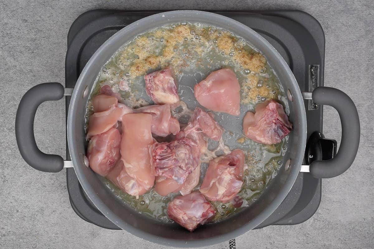 Pezzi di pollo aggiunti alla pentola, che rosolano nell'olio e nelle spezie.
