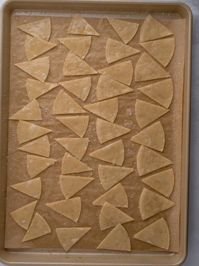 Tortillas di mais salate e oliate tagliate a triangoli su una teglia pronte per essere cotte.
