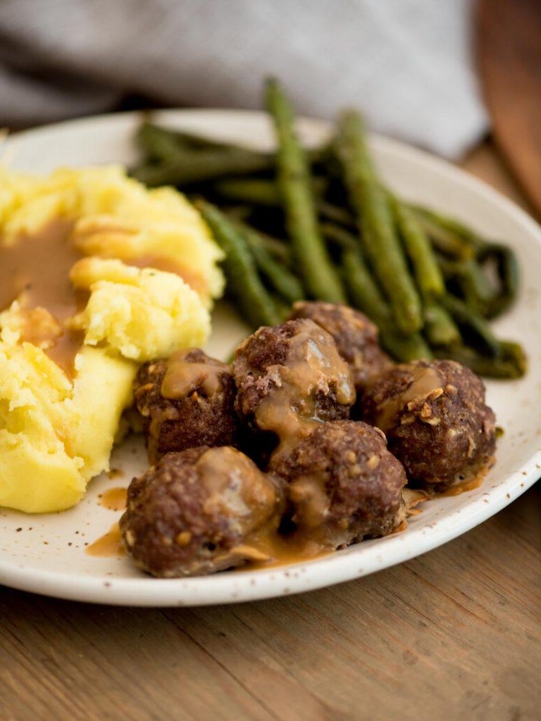 Polpette di cipolla alla francese con salsa gravy servite su un piatto con purè di patate e fagiolini arrostiti