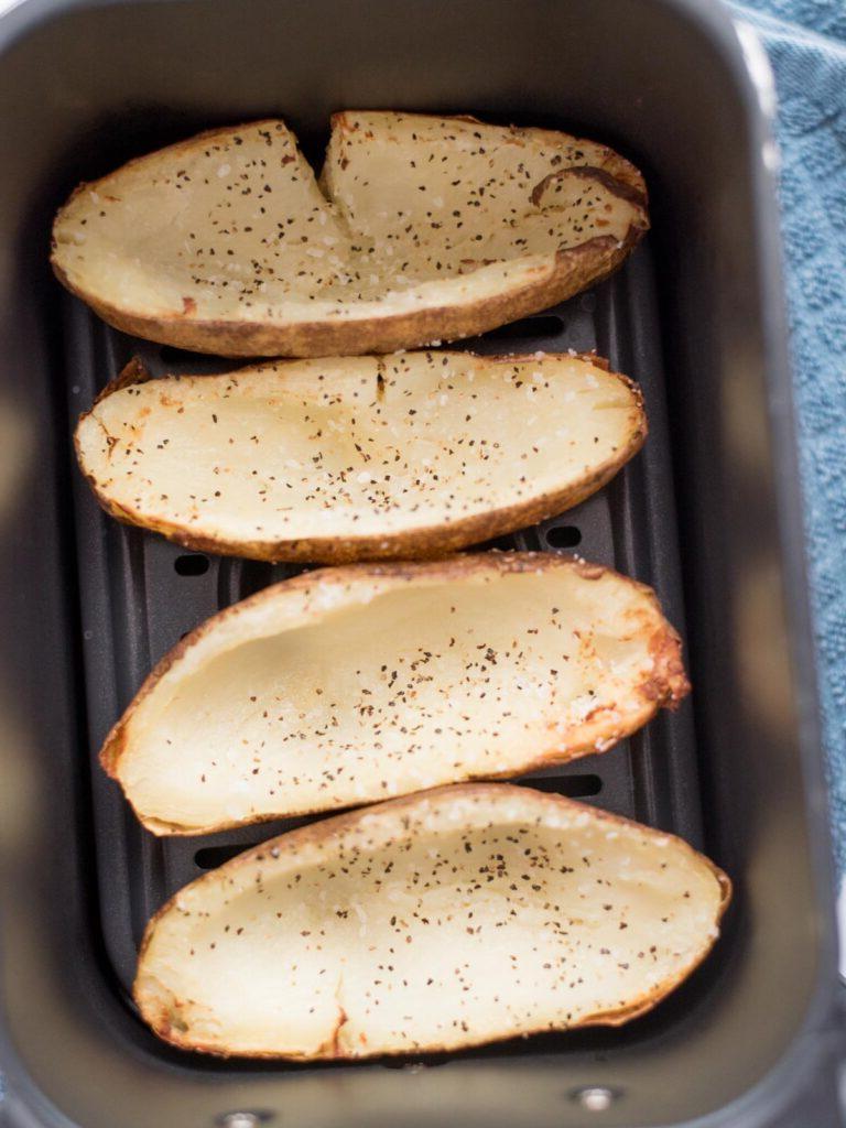Facili Bucce di Patate in Friggitrice ad Aria 8 4 patate russet con la polpa svuotata dal centro e condite con sale e pepe all'interno di un cestello della friggitrice ad aria.